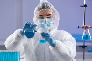 Scientist holding flasks with light blue liquid in laboratory