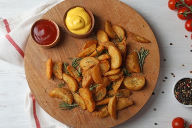 Photo of Baked potatoes served with rosemary, ketchup and mustard on table, top view