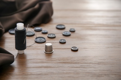 Thread, thimble and buttons for tailoring on wooden background