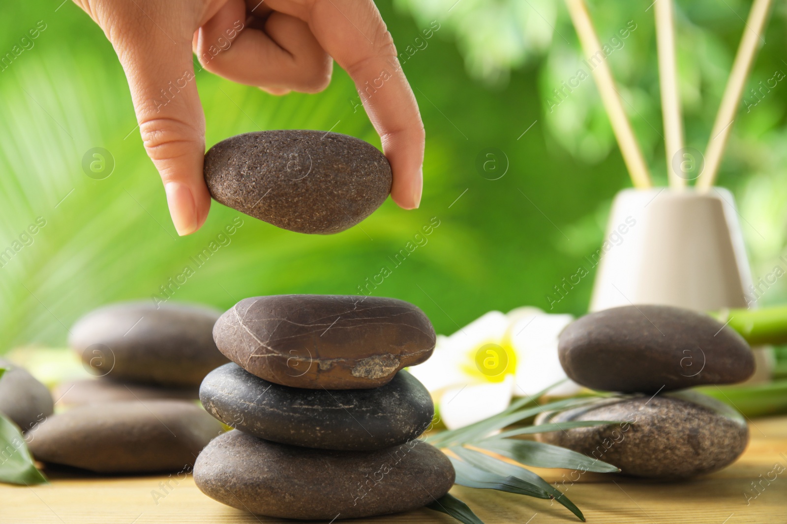 Photo of Woman stacking stones on table against blurred background, closeup. Zen concept