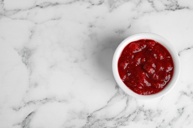 Photo of Bowl of cranberry sauce on marble background, top view. Space for text