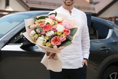 Young man with beautiful flower bouquet near car outdoors, closeup view