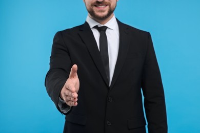 Man welcoming and offering handshake on light blue background, closeup