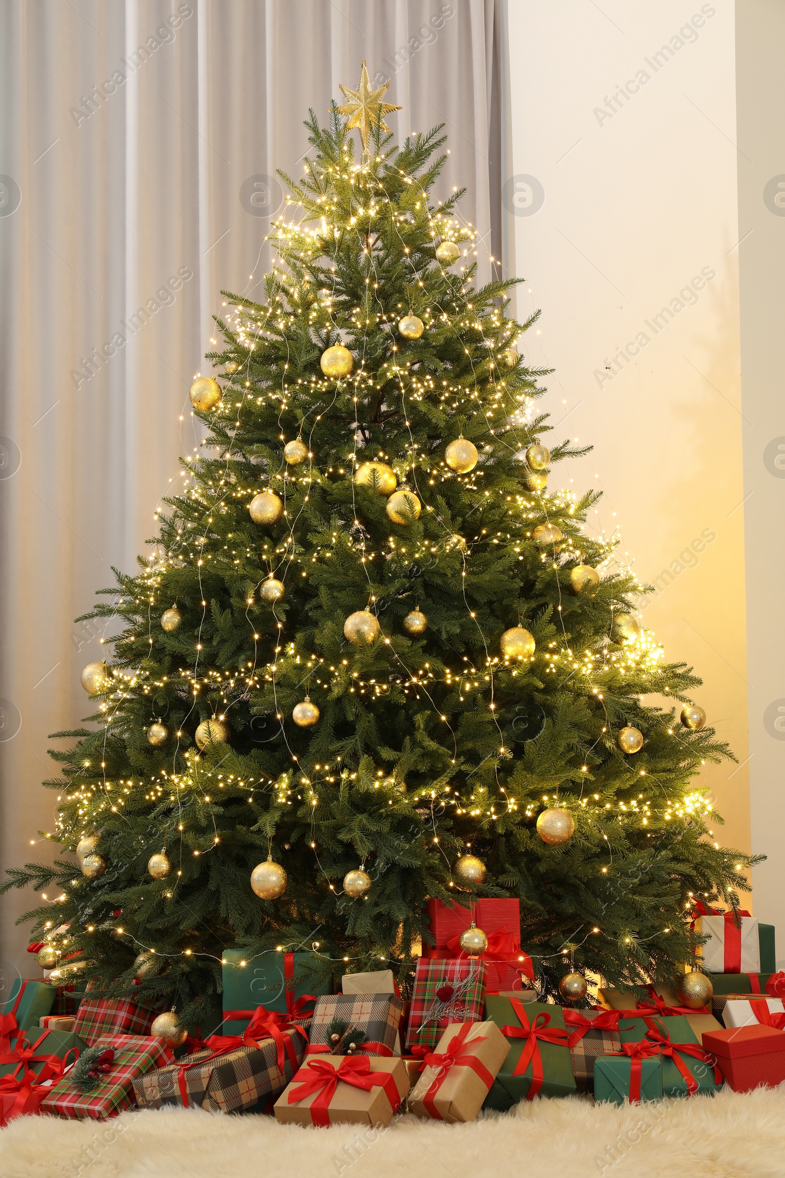 Photo of Many gift boxes under Christmas tree decorated with ornaments and festive lights in room