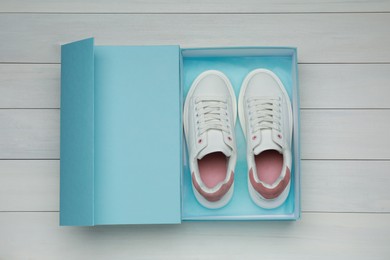 Pair of stylish sport shoes in turquoise box on white wooden background, top view