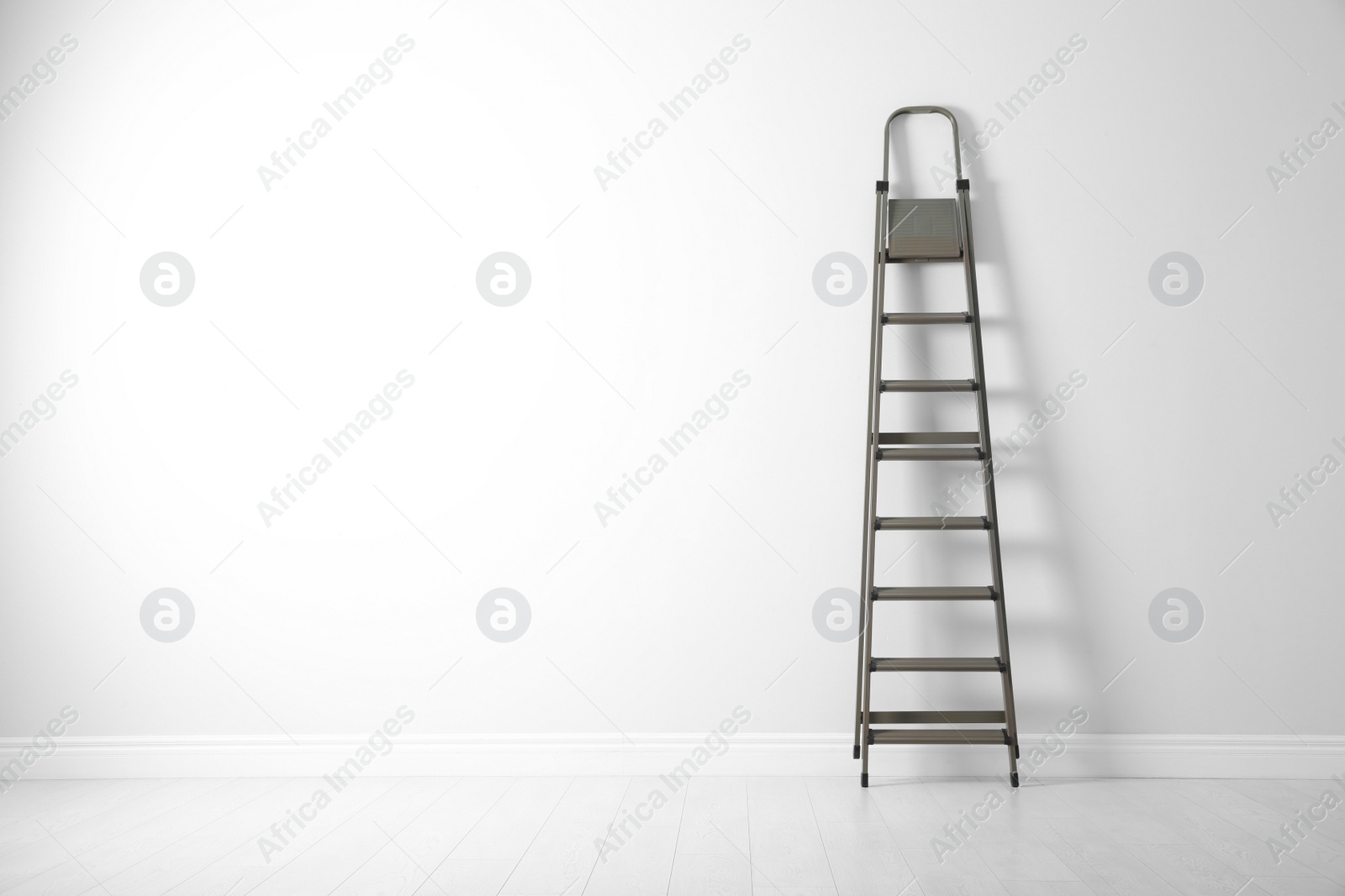 Photo of Modern metal stepladder near white wall. Space for text