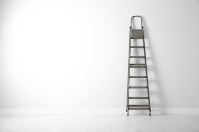 Modern metal stepladder near white wall. Space for text