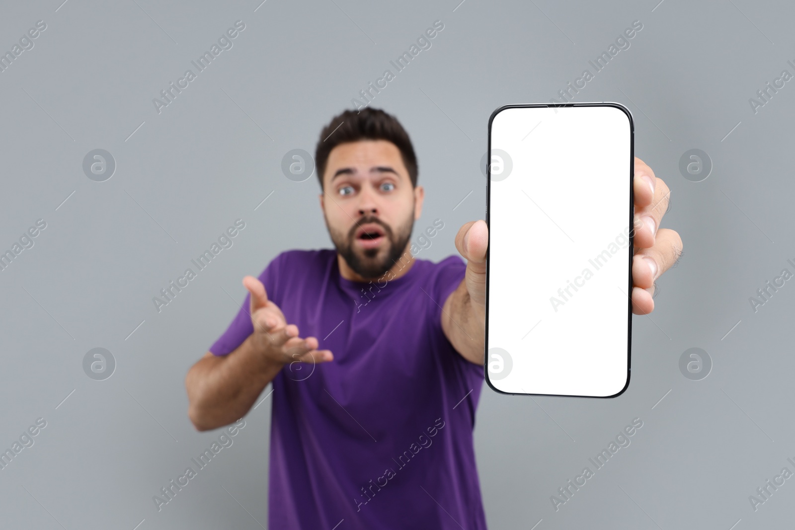 Photo of Surprised man showing smartphone in hand on light grey background, selective focus. Mockup for design