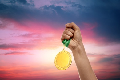 Winner raising hand with gold medal up to sunset sky, closeup