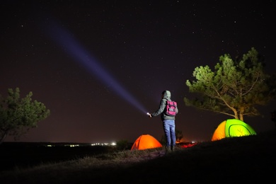 Photo of Man with bright flashlight near camping tents outdoors at night