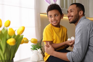 Photo of Happy African American father and his cute son with Easter eggs in kitchen