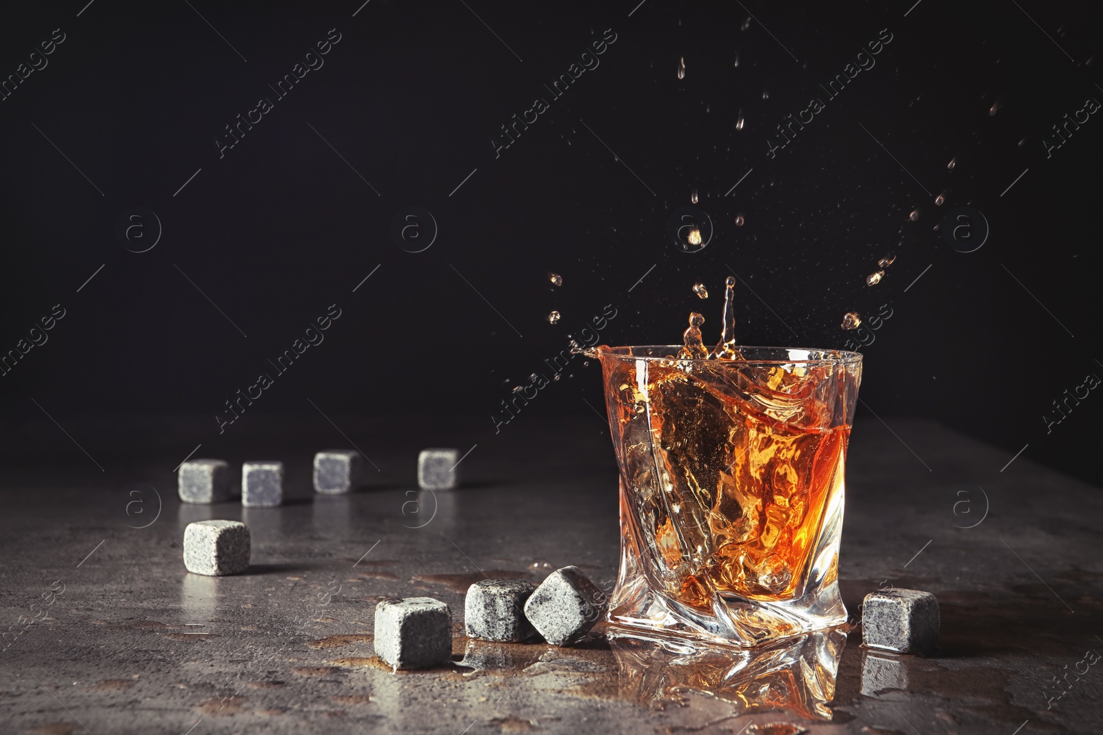 Photo of Glass with liquor splash and whiskey stones on table