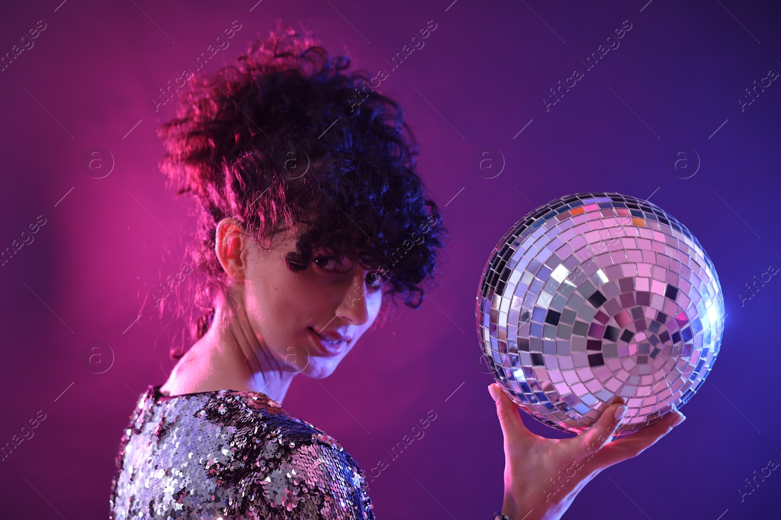 Photo of Beautiful young woman with disco ball posing on color background in neon lights