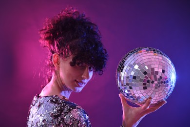 Beautiful young woman with disco ball posing on color background in neon lights