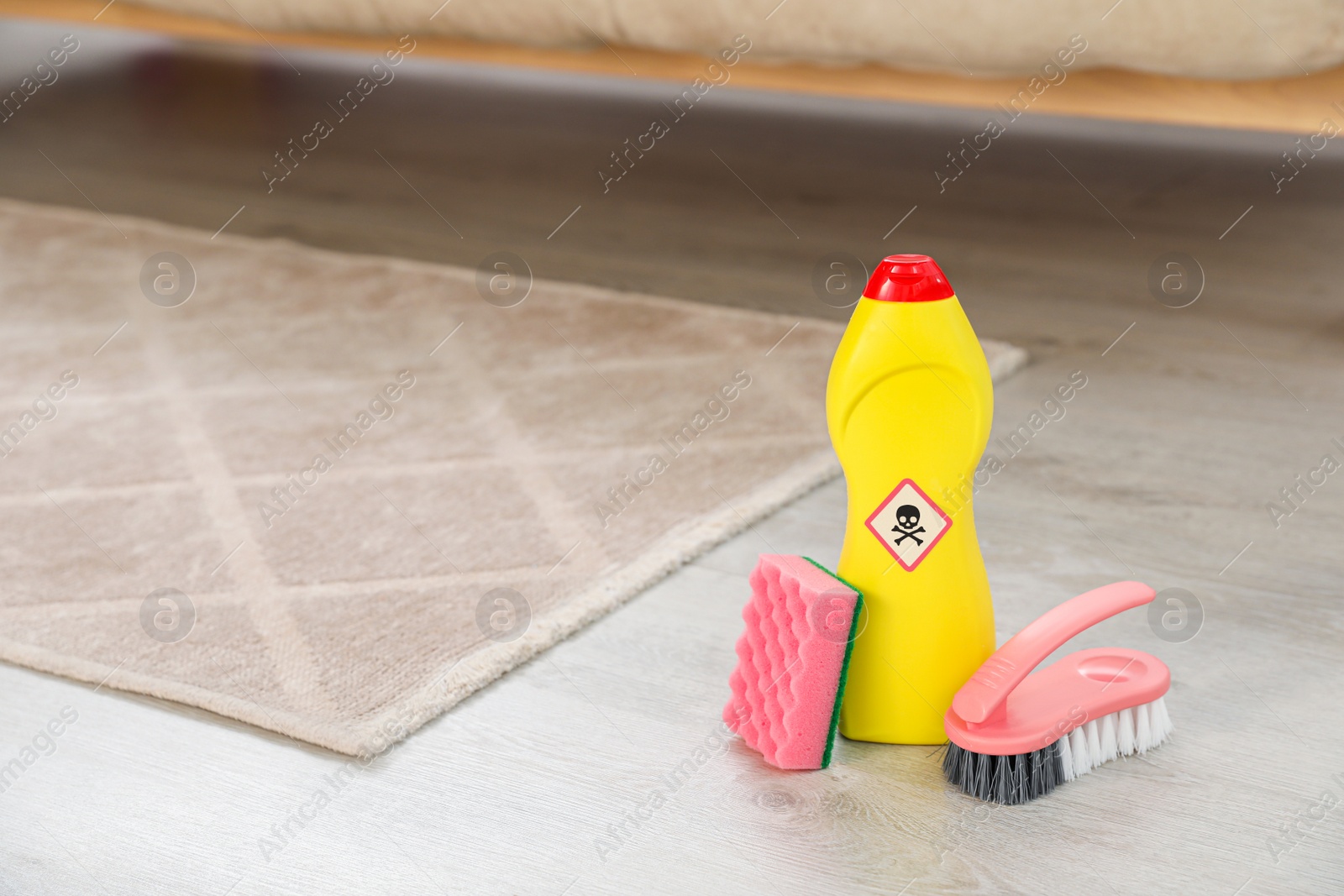 Photo of Bottle of toxic household chemical with warning sign, brush and scouring sponge in room, space for text