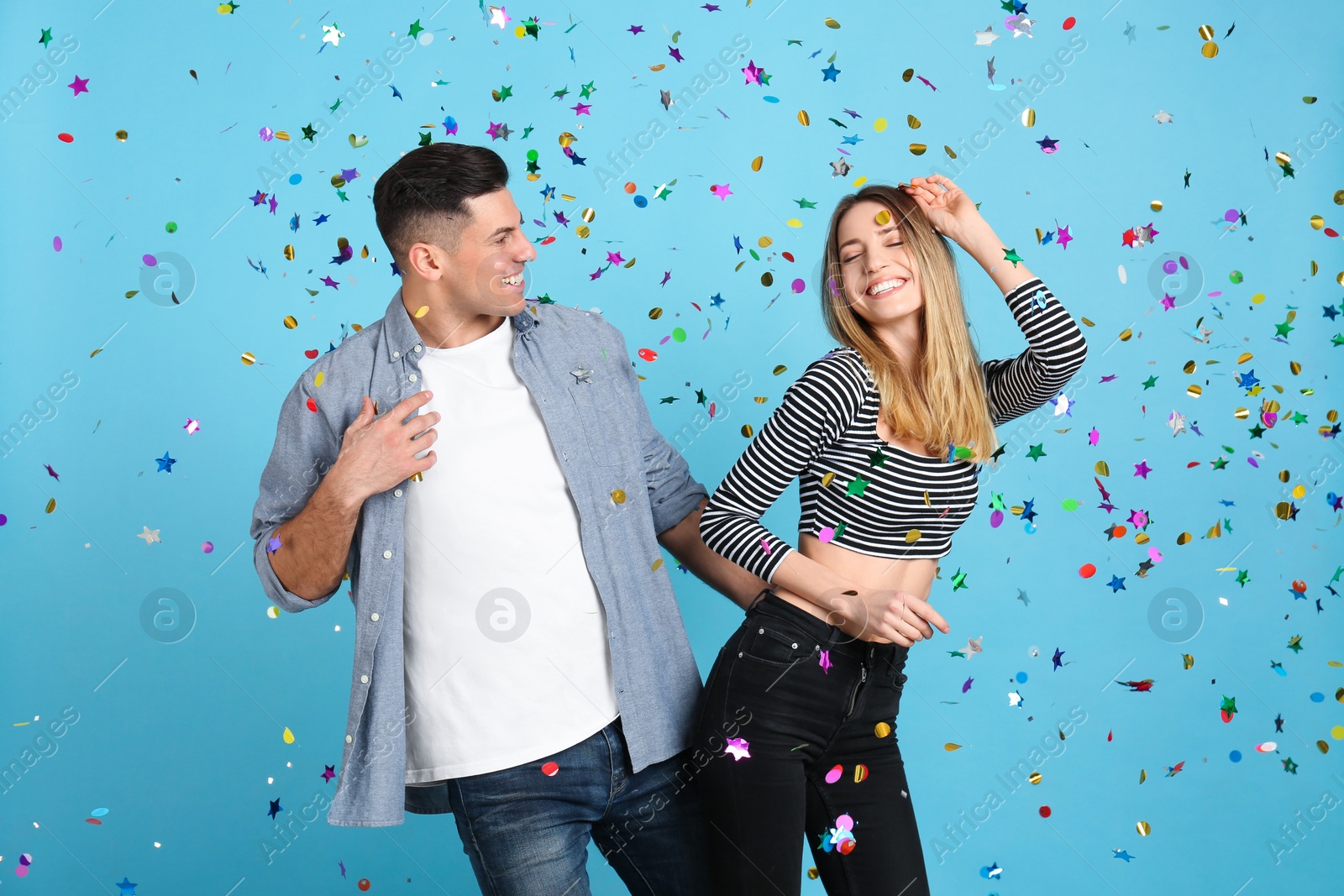 Photo of Happy couple and falling confetti on light blue background