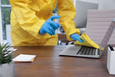 Photo of Janitor disinfecting laptop in office to prevent spreading of COVID-19