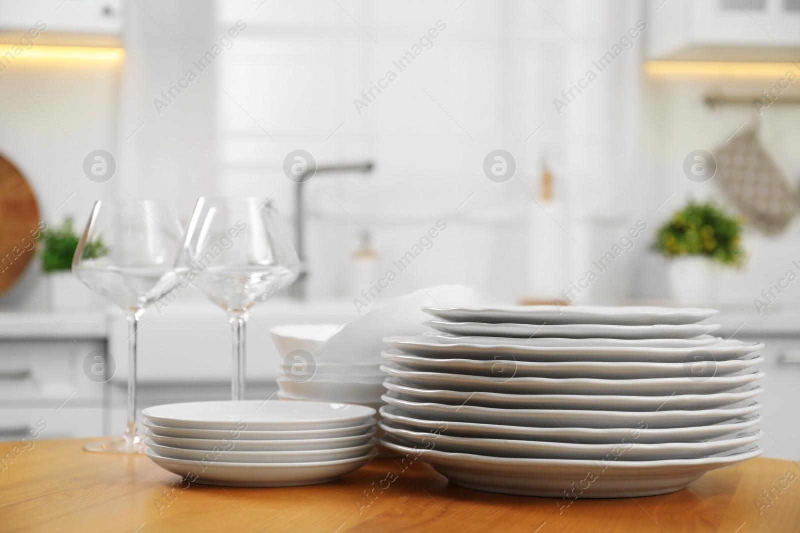 Photo of Clean plates, bowls and glasses on wooden table in kitchen