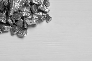 Photo of Pile of silver nuggets on white wooden table, top view. Space for text