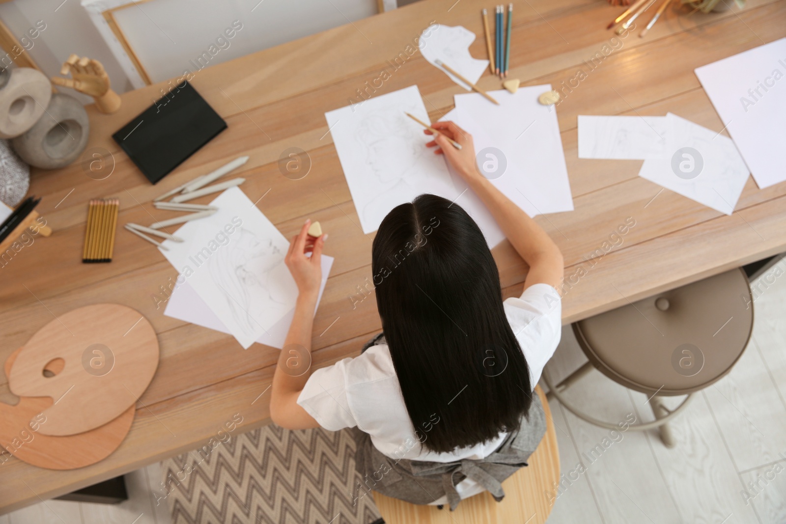 Photo of Young woman drawing male portrait at table indoors, top view