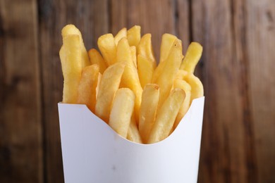 Delicious french fries in paper box on wooden background, closeup