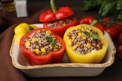 Photo of Quinoa stuffed bell peppers and basil in baking dish on table, closeup