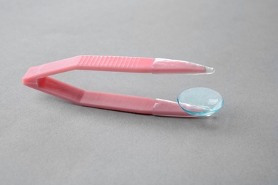 Photo of Tweezers with contact lens on light background