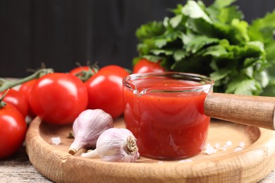 Delicious ketchup, salt and garlic on wooden table, closeup. Tomato sauce