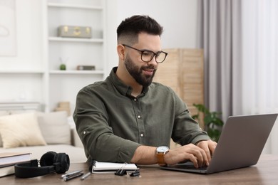 Photo of E-learning. Young man using laptop during online lesson at wooden table indoors