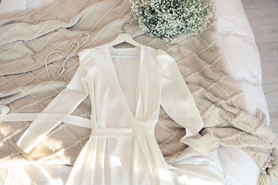 Photo of White wedding dress, beautiful bouquet and pearl necklace on bed in room