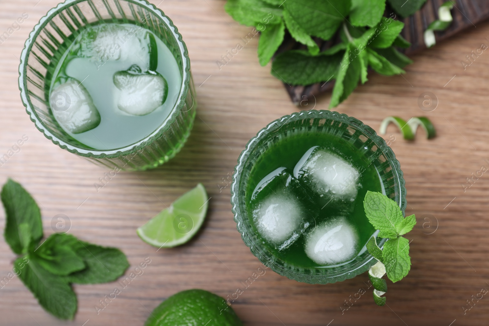 Photo of Delicious mint liqueur with green leaves and ice cubes on wooden table, flat lay