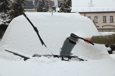 Woman cleaning car windshield from snow with brush outdoors, closeup