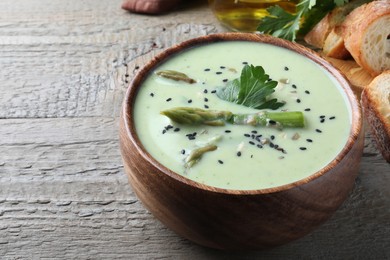 Photo of Bowl of delicious asparagus soup on wooden table, space for text