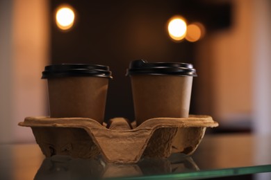 Takeaway coffee cups with cardboard holder on glass table indoors, closeup