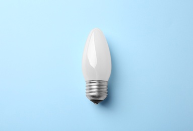 New modern lamp bulb on light blue background, top view