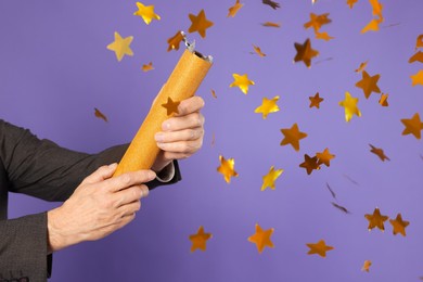 Man blowing up party popper on purple background, closeup