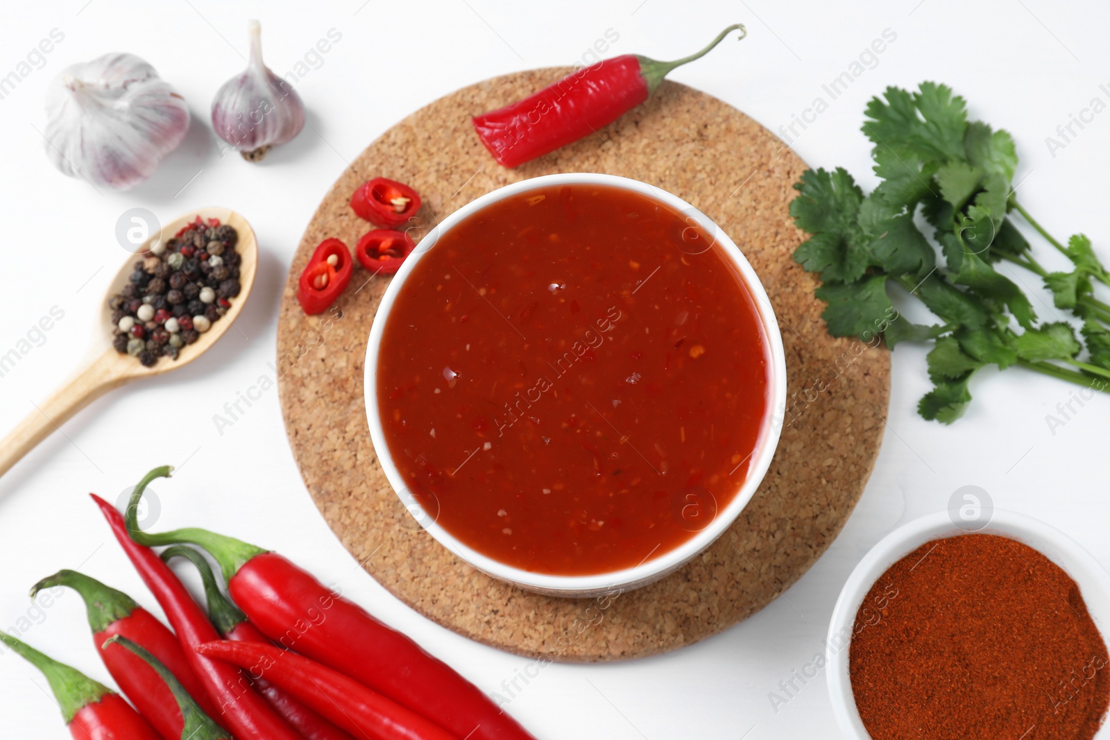 Photo of Spicy chili sauce in bowl and ingredients on white background, flat lay