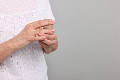 Arthritis symptoms. Woman suffering from pain in fingers on gray background, closeup. Space for text