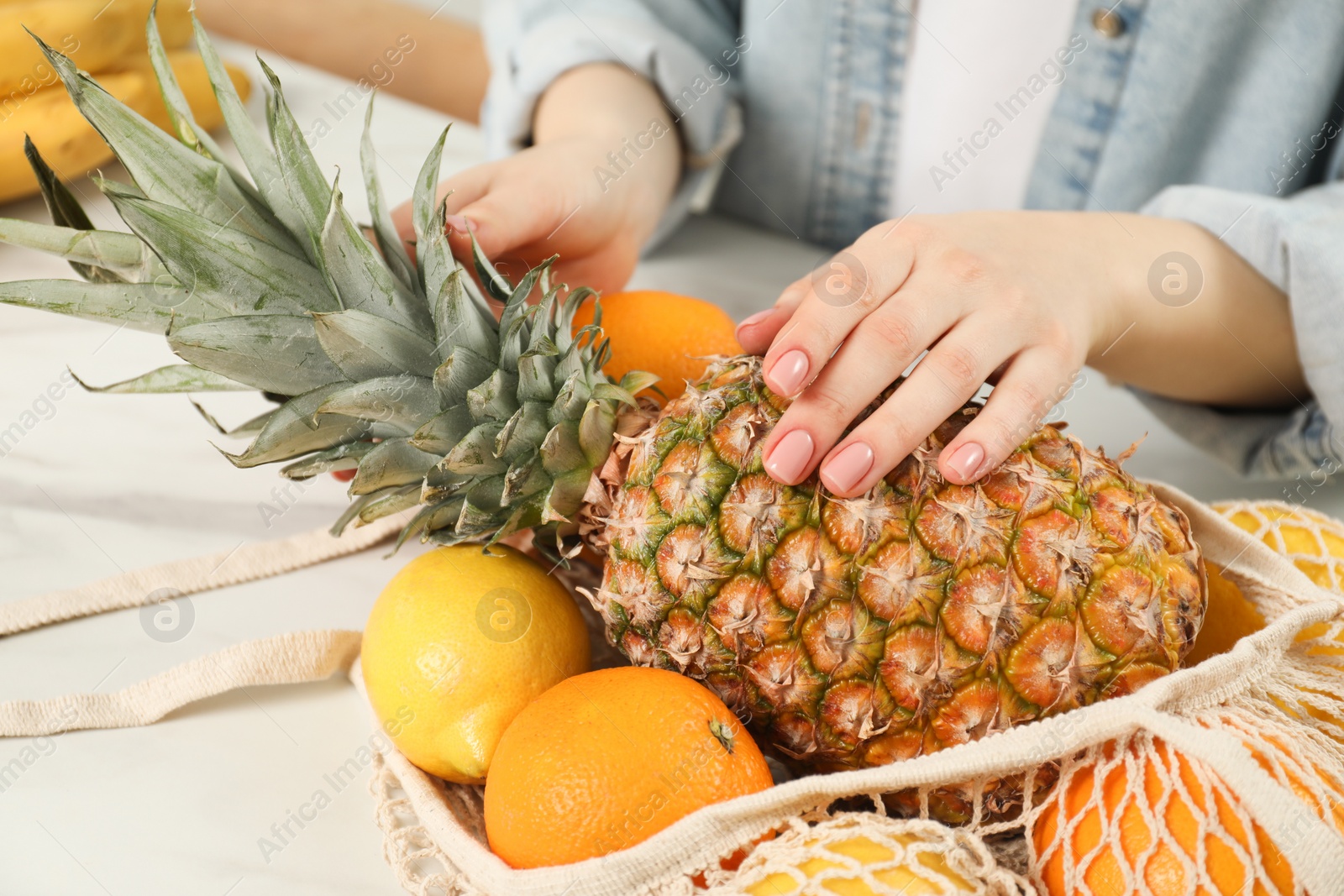 Photo of Woman with string bag of fresh fruits at light table, closeup