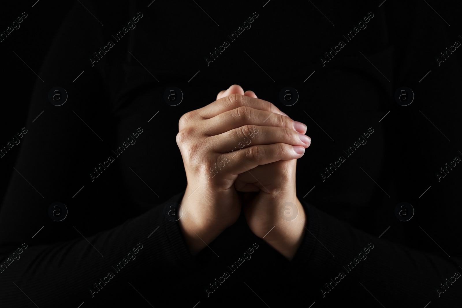 Photo of Woman holding hands clasped while praying in darkness, closeup