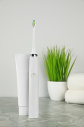 Photo of Electric toothbrush and tube with paste on light grey marble table