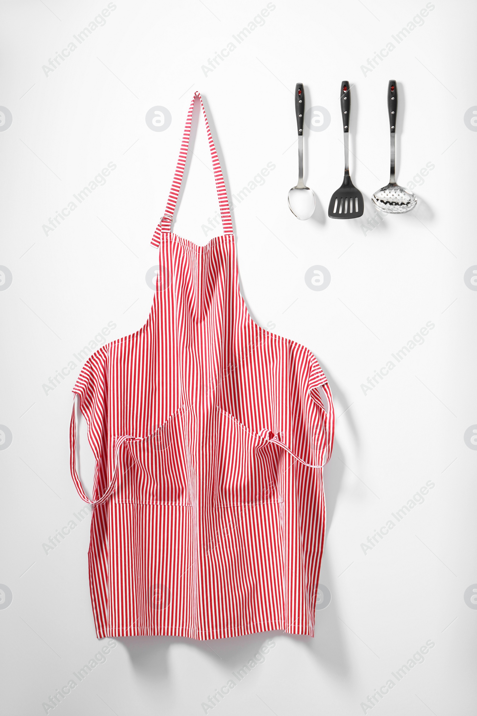 Photo of Red striped apron and kitchen tools on light wall