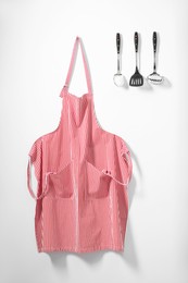 Photo of Red striped apron and kitchen tools on light wall