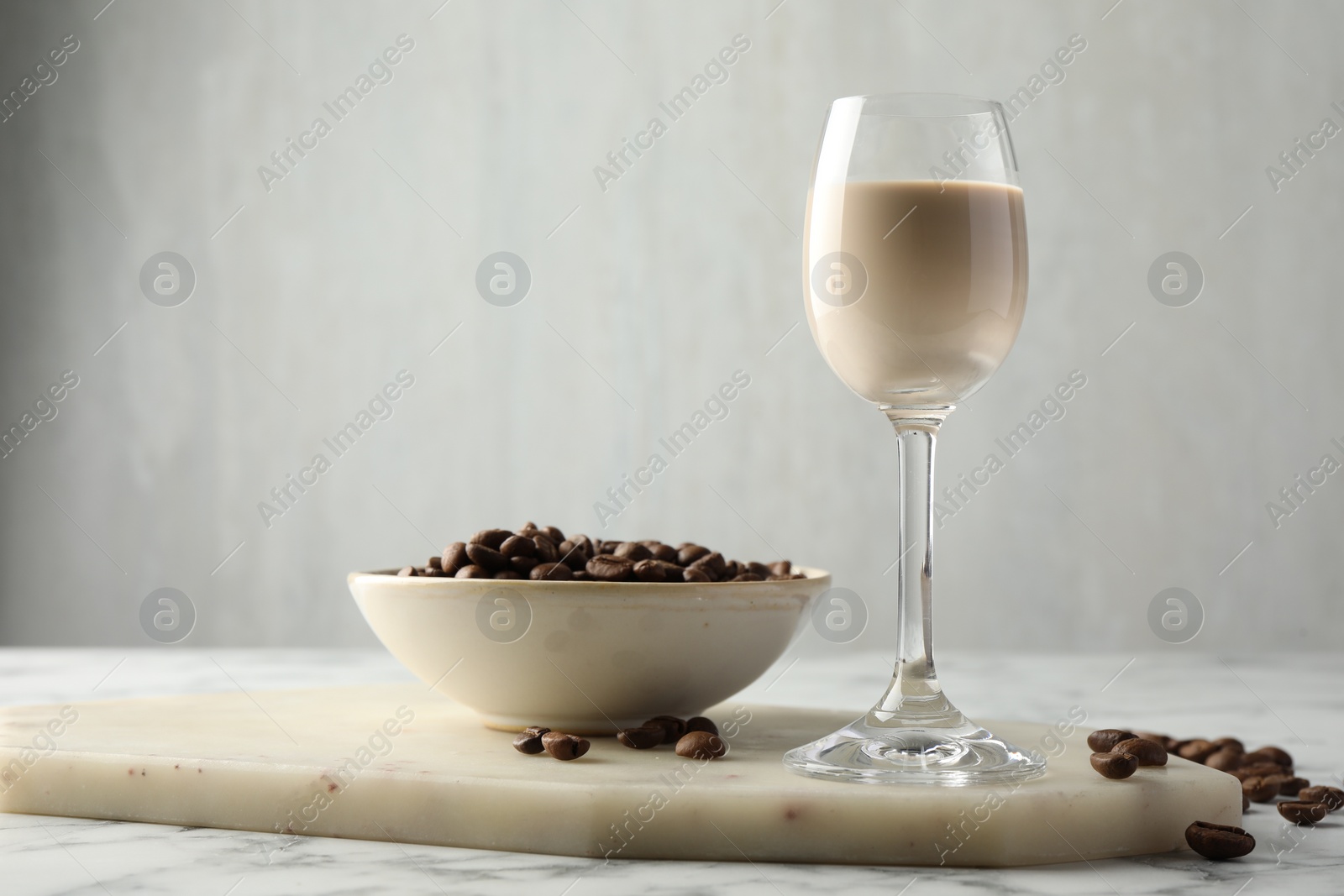 Photo of Coffee cream liqueur in glass and beans on white marble table