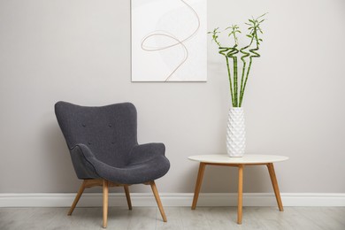 Vase with green bamboo stems and stylish armchair in room. Interior design