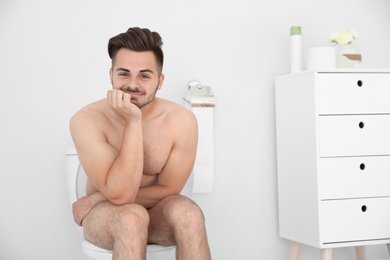 Photo of Young naked man sitting on toilet bowl at home
