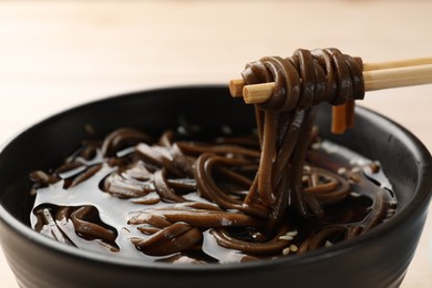 Photo of Eating delicious buckwheat noodle (soba) soup with chopsticks at table, closeup