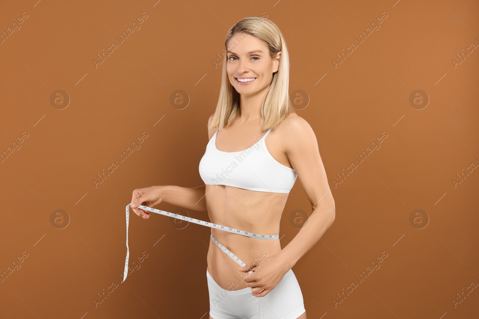 Photo of Slim woman measuring waist with tape on brown background. Weight loss