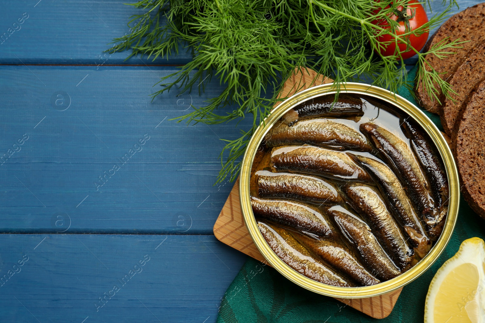 Photo of Tin can with tasty sprats served on blue wooden table, flat lay. Space for text