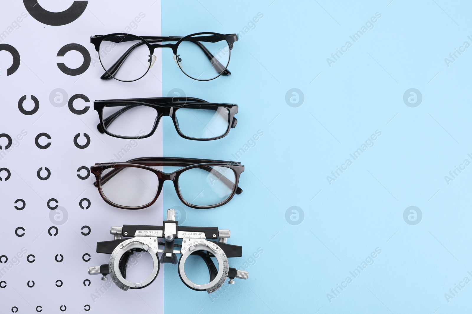 Photo of Vision test chart, glasses and trial frame on light blue background, flat lay. Space for text